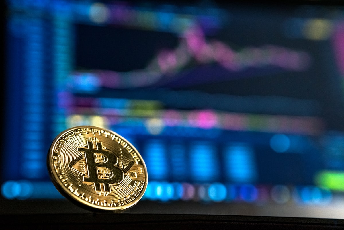 Gold bitcoin coin in front of financial trading charts representing bitcoin retirement tax strategy